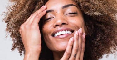 Mulher negra sorrindo com as mãos no rosto.