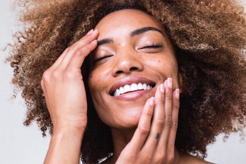 Mulher negra sorrindo com as mãos no rosto.