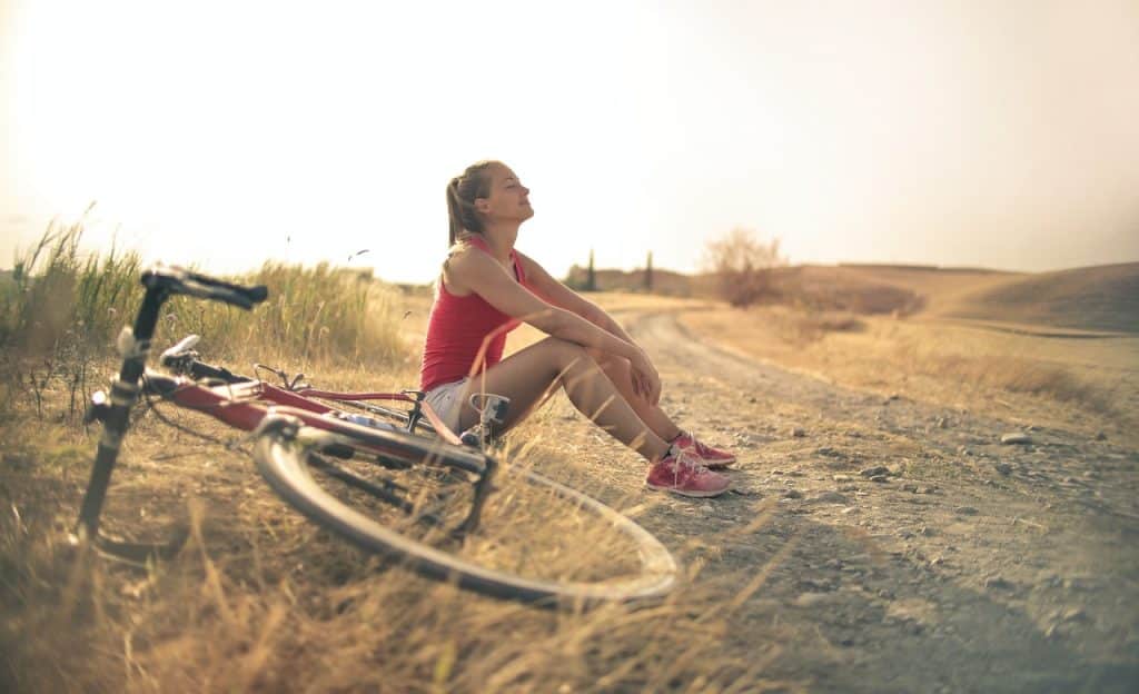 Mulher sentada em uma estrala rural. Ao lado dela, há uma bicicleta deitada.