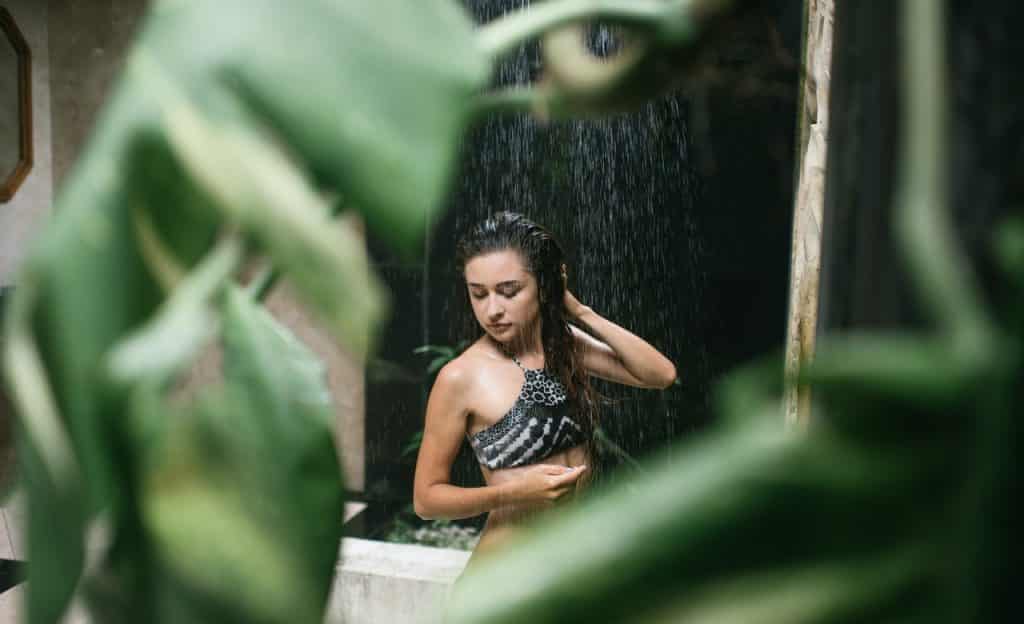 Mulher toma banho; sobre a sua imagem há uma planta.