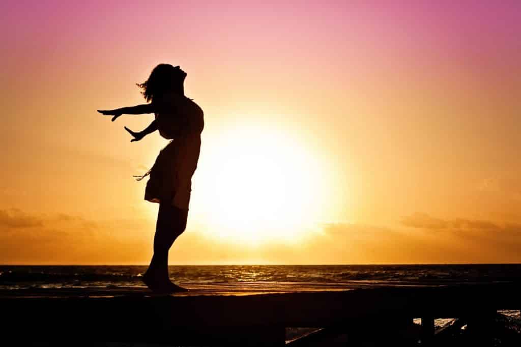 Silhueta de uma mulher na praia com o sol se pondo ao fundo.