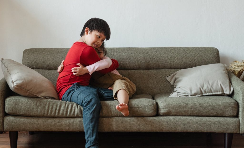 Duas crianças sentadas em um sofá se abraçam.