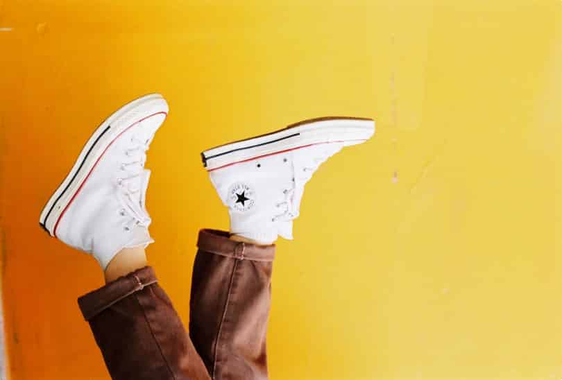 Plano de fundo amarelo com pés calçando sapatos brancos à frente