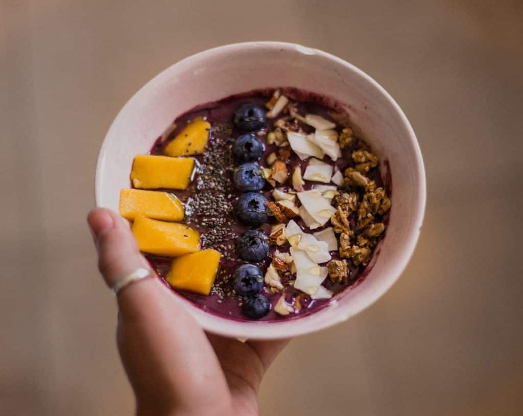 Mulher negra segurando bowl com açaí e frutas.