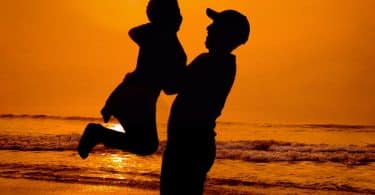Silhueta de homem segurando criança numa praia.