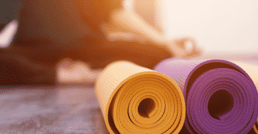 Pessoa meditando com tapetes de yoga dobrados na frente