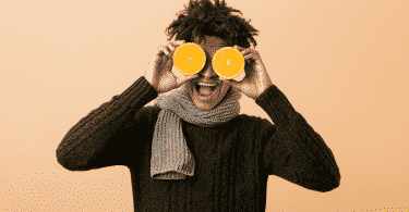 Homem sorridente segurando duas metades de laranjas na frente dos olhos
