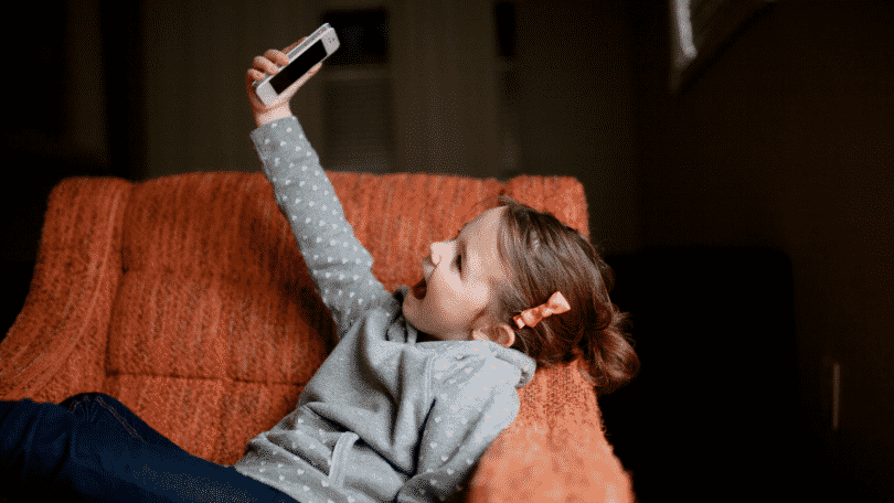 Criança deitada no sofá sorrindo tirando uma selfie