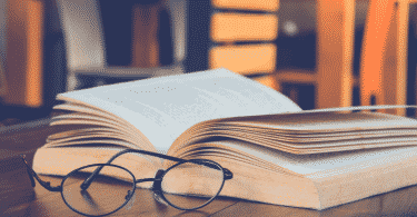 Livros abertos sob a mesa com óculos de leitura ao lado