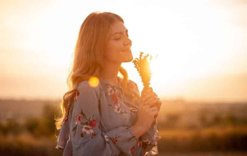 Mulher branca de olhos fechados segurando ramo de flores.