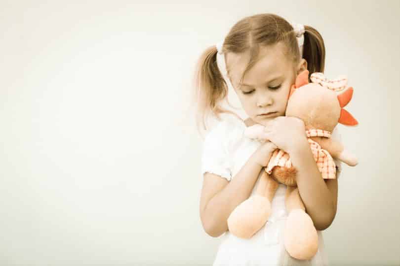 Garota triste segurando um urso de pelúcia.