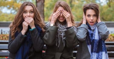 Mulheres brancas sentadas com as mãos na boca, olhos e orelhas.