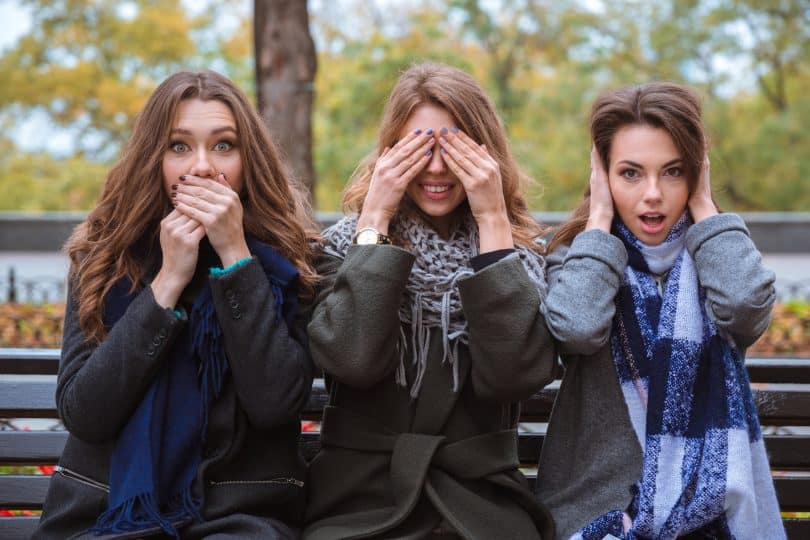 Mulheres brancas sentadas com as mãos na boca, olhos e orelhas.