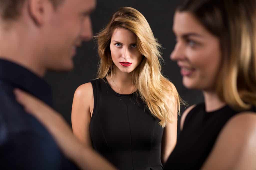 Mulher com ciúme olhando para seu namorado conversando com outra mulher.