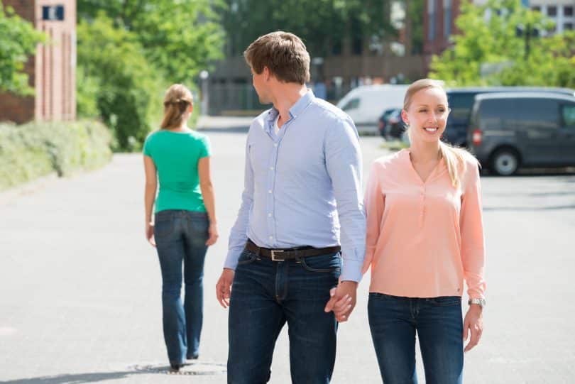 Jovem caminhando com a namorada na rua, olhando para outra mulher