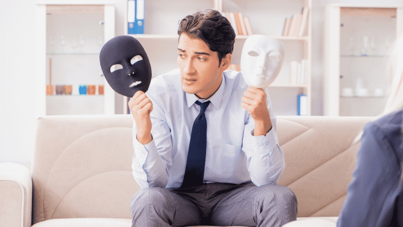 Homem sentado segurando duas máscaras, uma branca e outra preta
