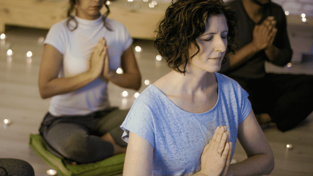 Pessoas com os olhos fechados e mãos juntas, meditando.