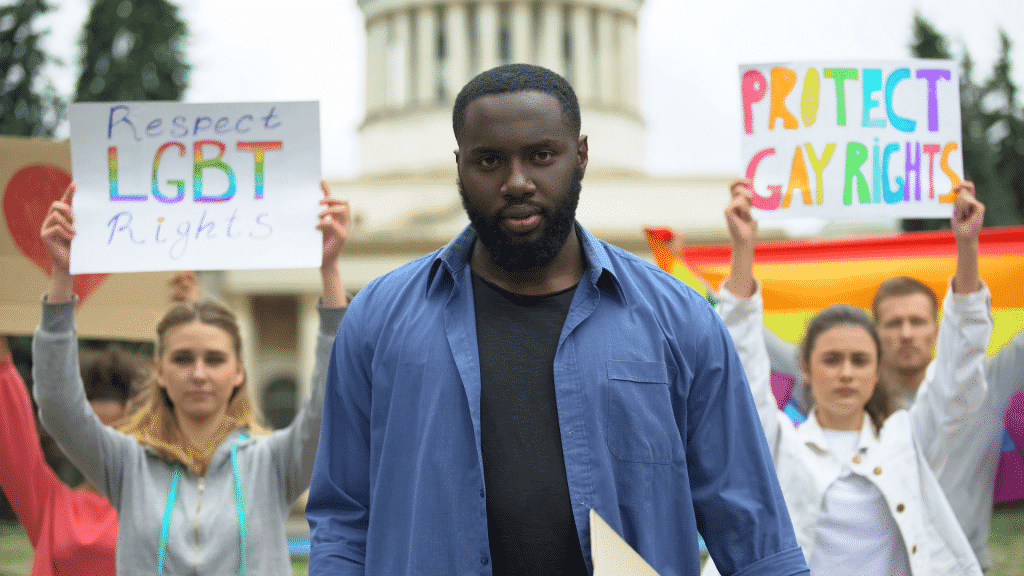 Homem e mulheres em uma passeata segurando placas, pedindo respeito e proteção aos direitos LGBTQIA+