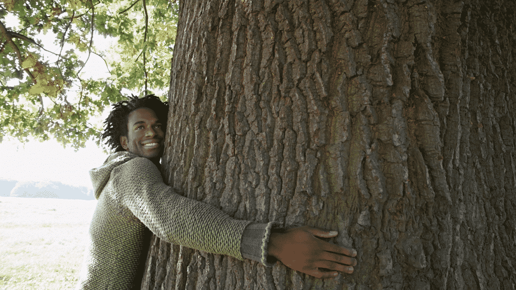 Homem sorrindo e abraçando uma árvore