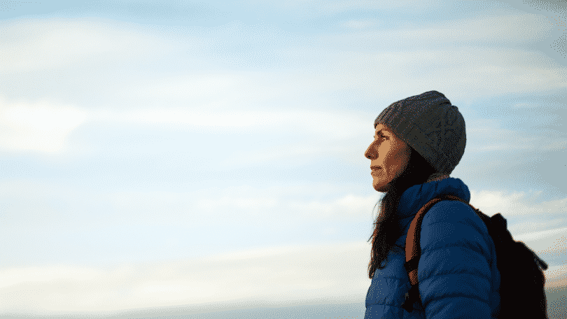 Mulher com roupas de frio e mochila olhando para o horizonte