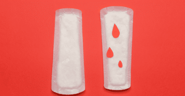 Absorventes com pingos de sangue em fundo vermelho.