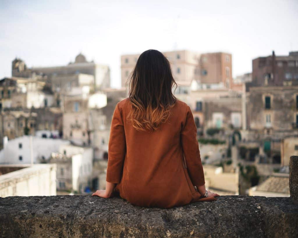 Mulher branca sentada no parapeito de um prédio.