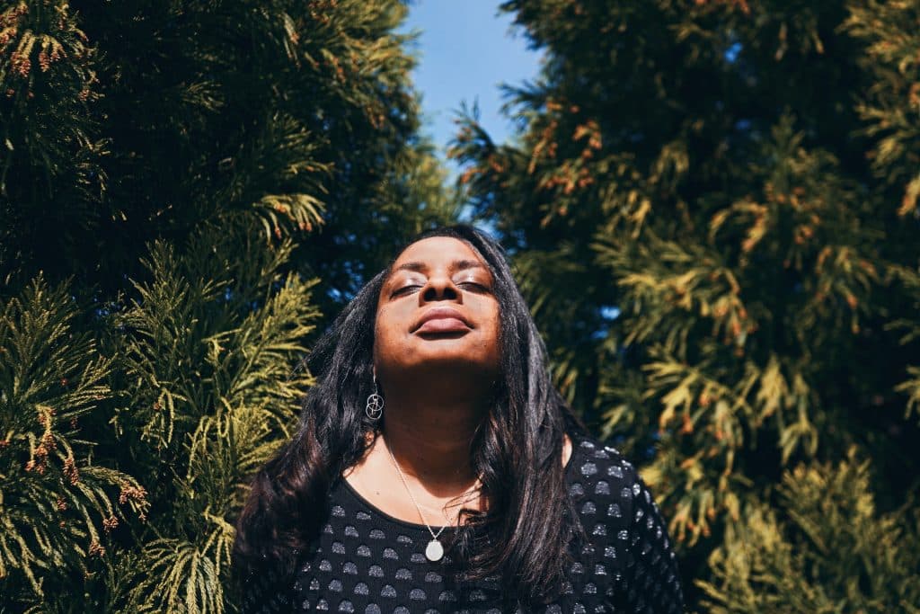 Mulher negra de olhos fechados e plantas atrás.