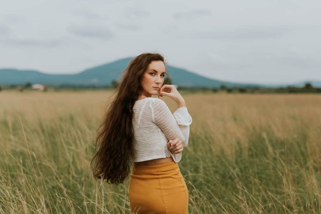 Mulher branca com a mão no rosto e olhando para trás num campo.