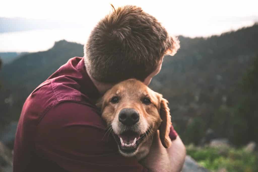 Homem branco abraçando cachorro.