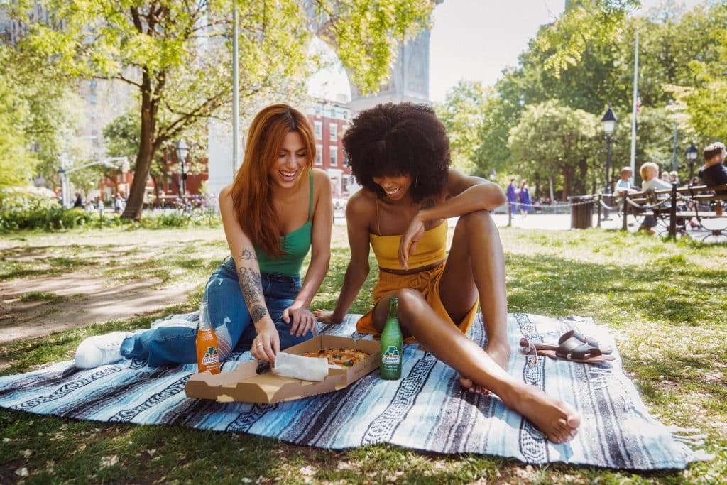 Mulheres branca e negra comendo pizza na grama.