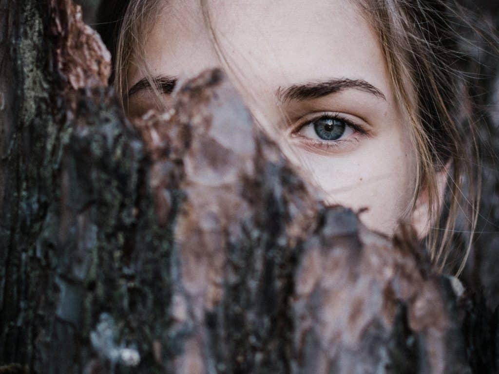 Foco nos olhos de uma mulher que está atrás de um troco de árvore