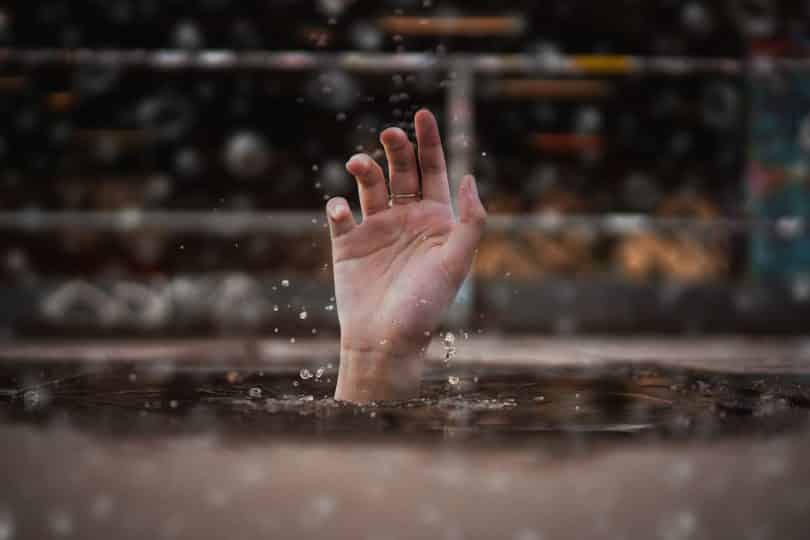 Uma pessoa se afogando esticando sua mão acima do nível da água