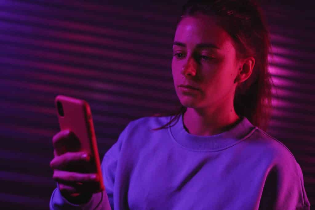 Menina olhando para o celular com semblante triste.