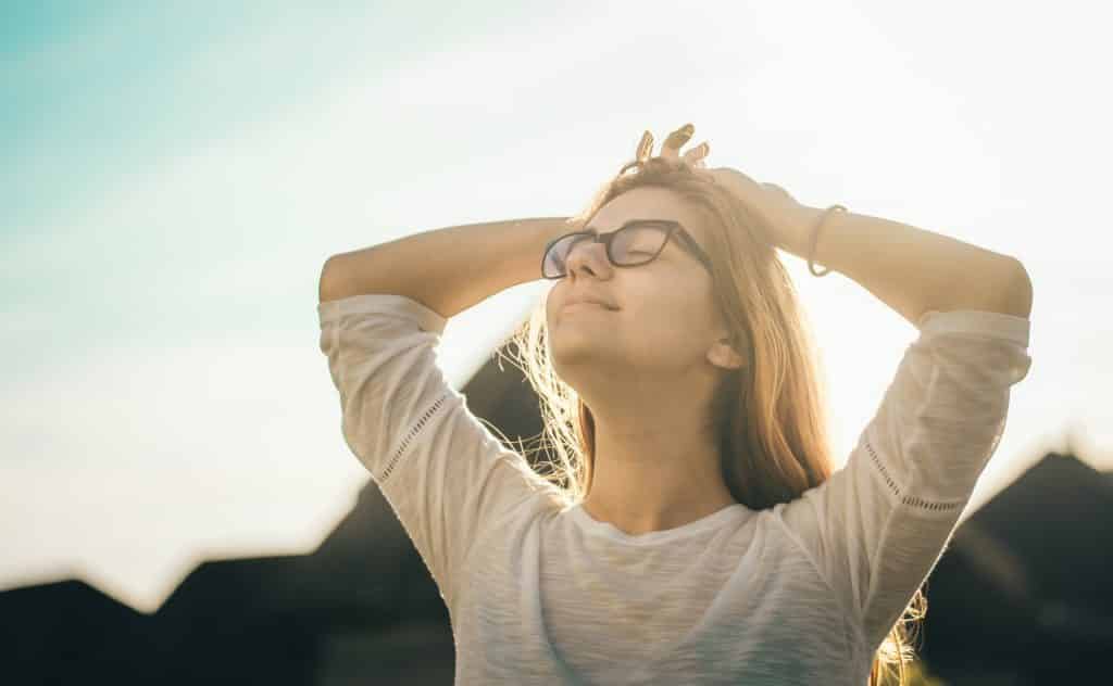 Mulher branca com as mãos na cabeça e olhos fechados.