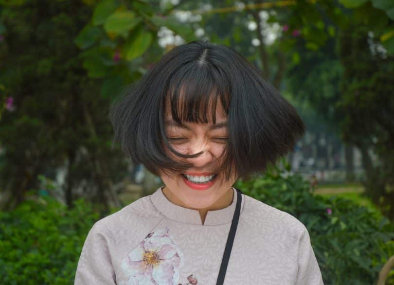 Mulher asiática sorrindo e com os cabelos balançando.