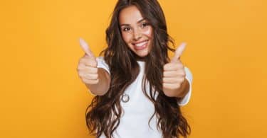 Mulher jovem feliz isolada sobre fundo amarelo, mostrando os polegares para cima gesto.