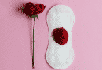 Uma rosa à esquerda. À direita, um absorvente com pétalas de rosa em cima.