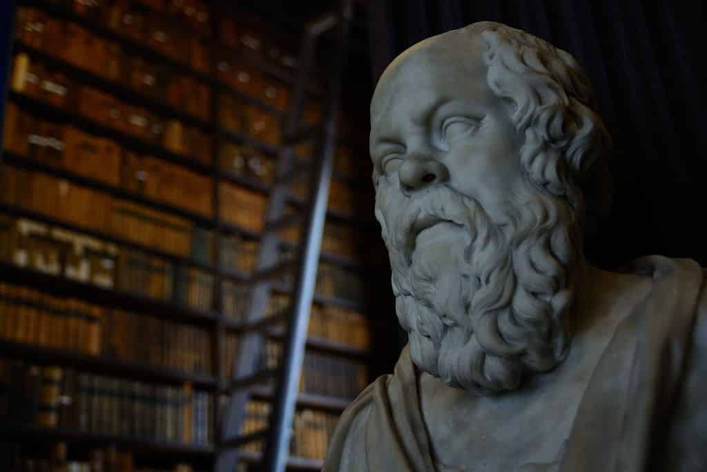 Um busto de Sócrates. Ao fundo, prateleiras de livros.