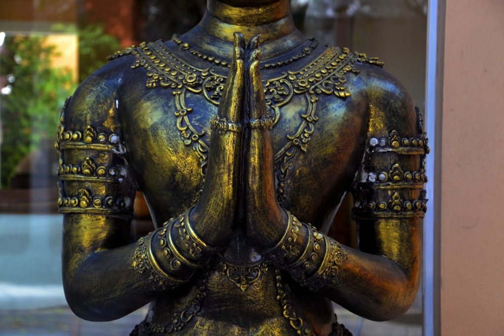 Uma estátua budista em bronze. Ela cerra as mãos em um gesto de oração.