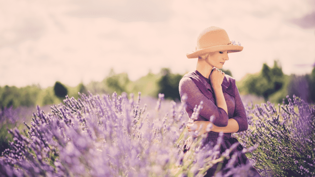 Mulher de chapéu e vestido roxo no meio de um campo com flores roxas