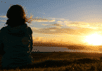 Mulher sentada em um campo observando o sol