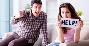 Um homem sentado à esquerda, bravo. À direita, uma mulher também sentada, segurando uma placa escrito "help!"