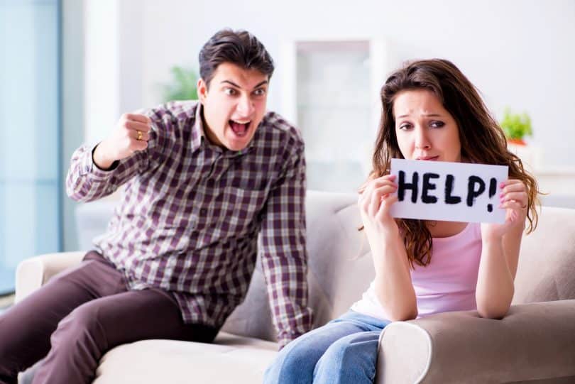 Um homem sentado à esquerda, bravo. À direita, uma mulher também sentada, segurando uma placa escrito "help!"