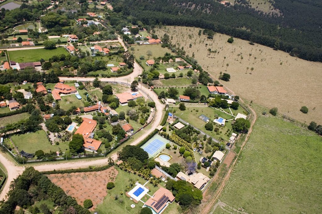 Uma vista aérea e panorâmica da cidade da Cabreúva. Nela há casas dispersas e à direita uma reserva verde, repleta de árvores.