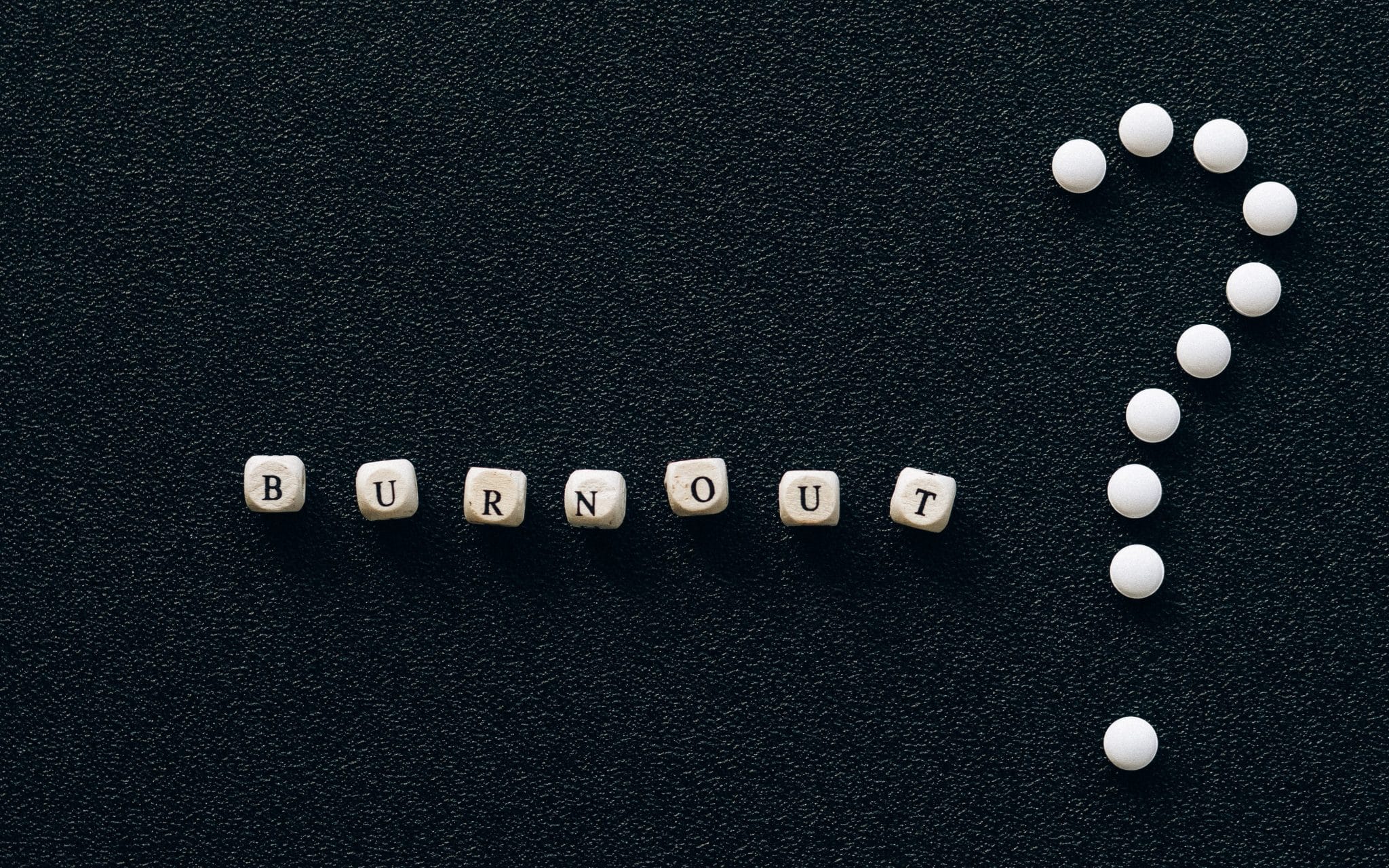 Dados com as letras da palavra BURNOUT. Ao lado direito, pequenas esferas que formam um ponto de interrogação.