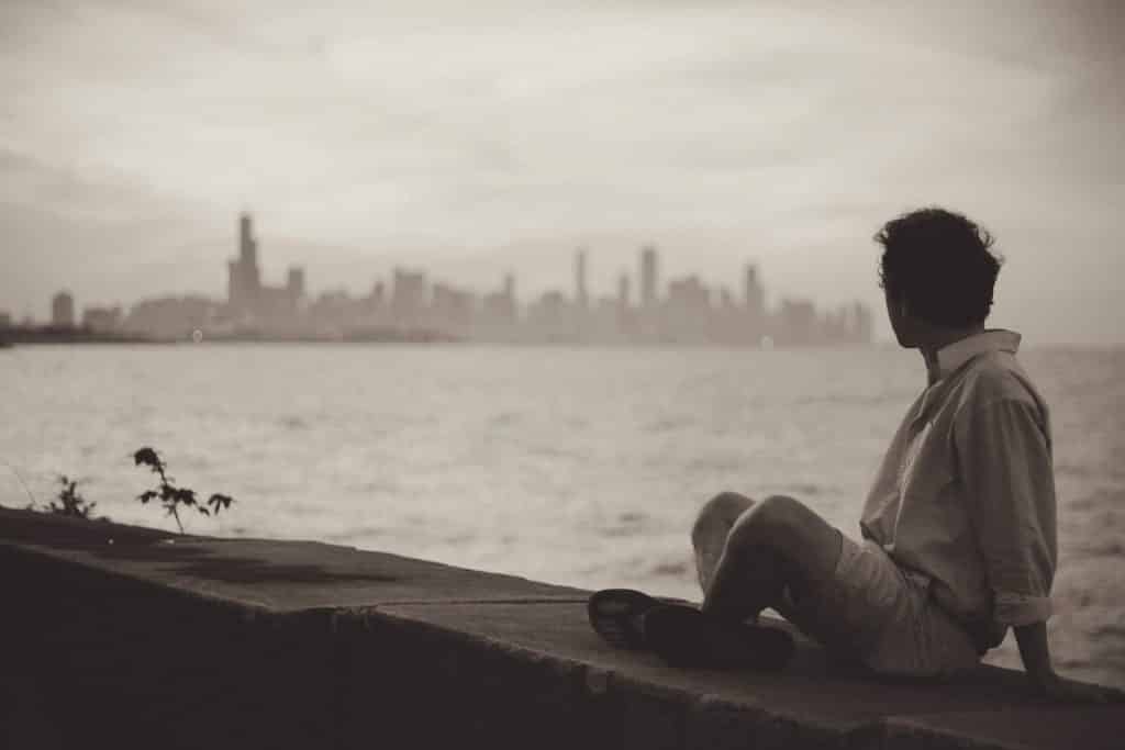 Um homem contemplando, a distância, uma zona urbana grande/uma cidade. Dividindo ambos, um grande rio.