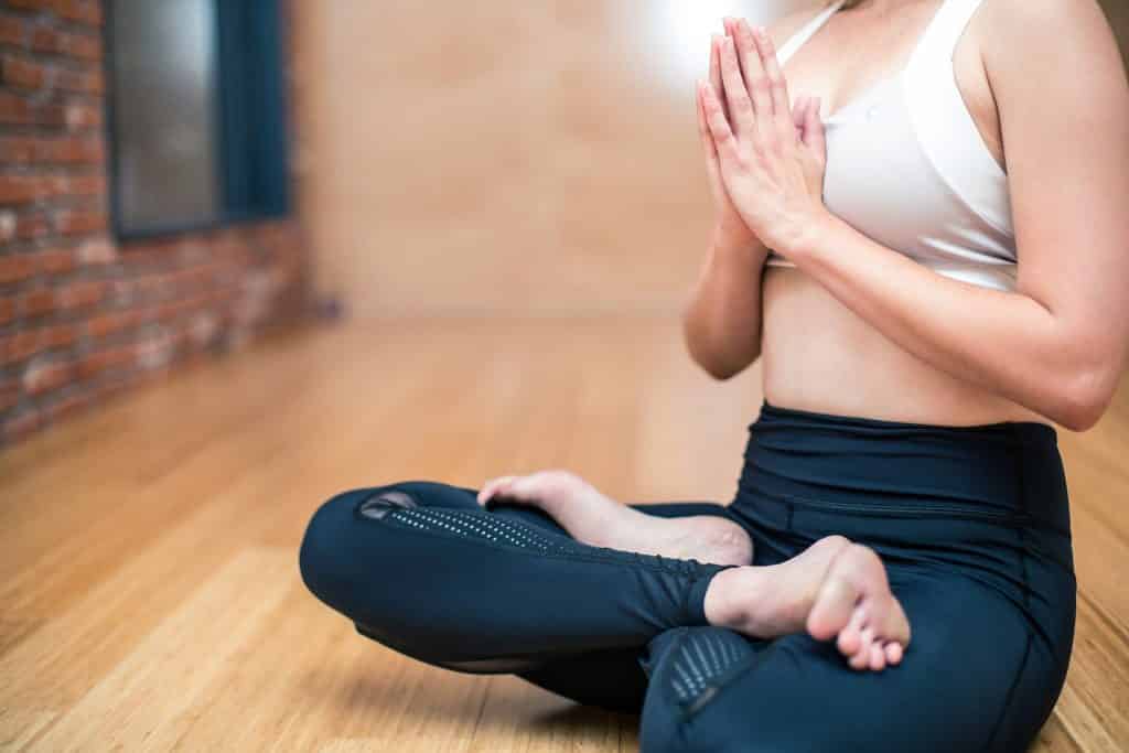 Uma mulher de blusa branca e calças leggings preta fazendo yoga.