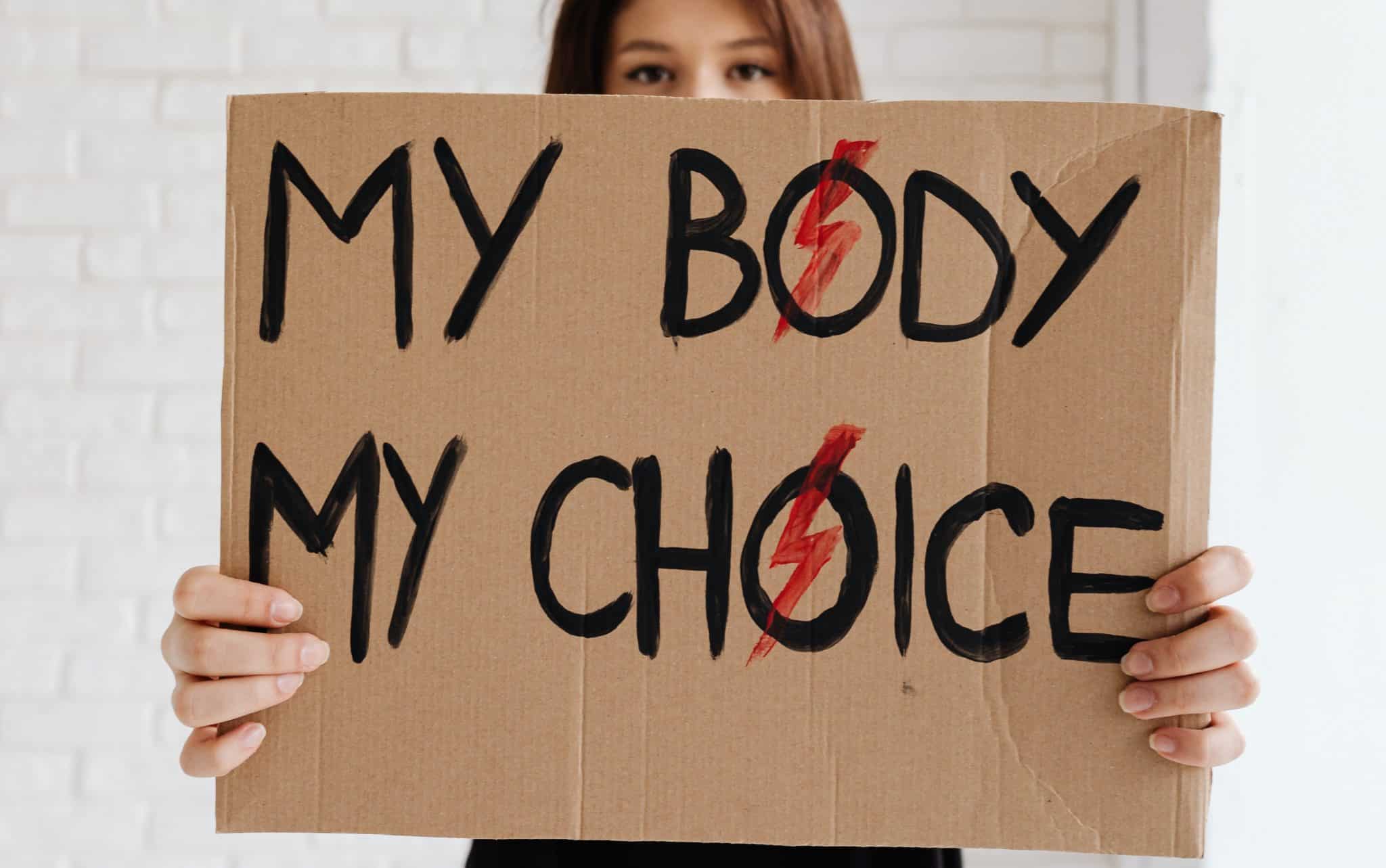 Uma mulher segurando uma placa de papelão escrita "my body my choice".