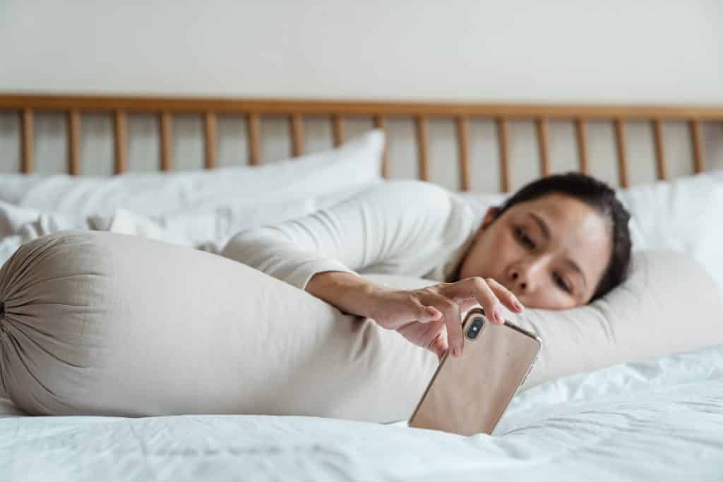 Uma mulher deitada numa cama observando um celular