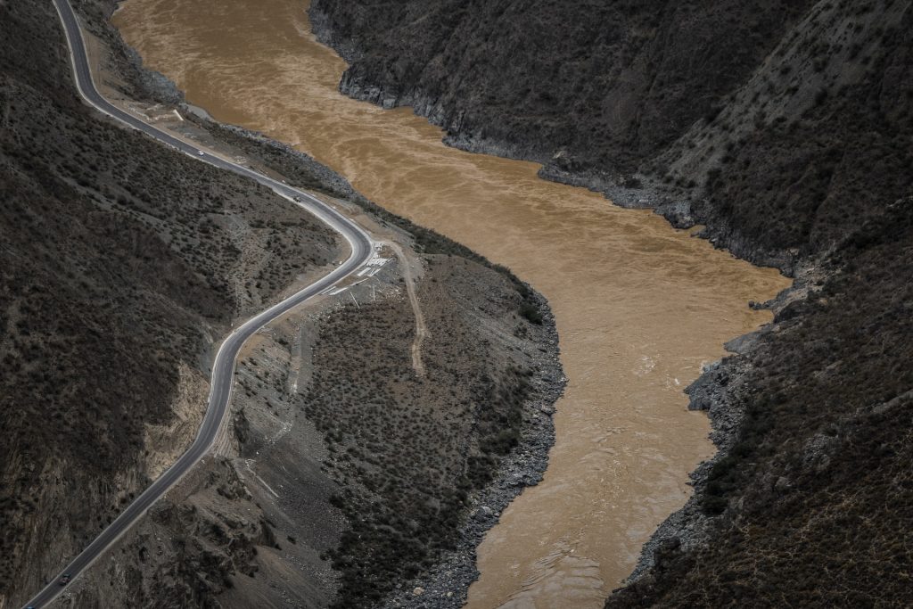 Um extenso rio poluído visto de cima, À esquerda, uma estrada.